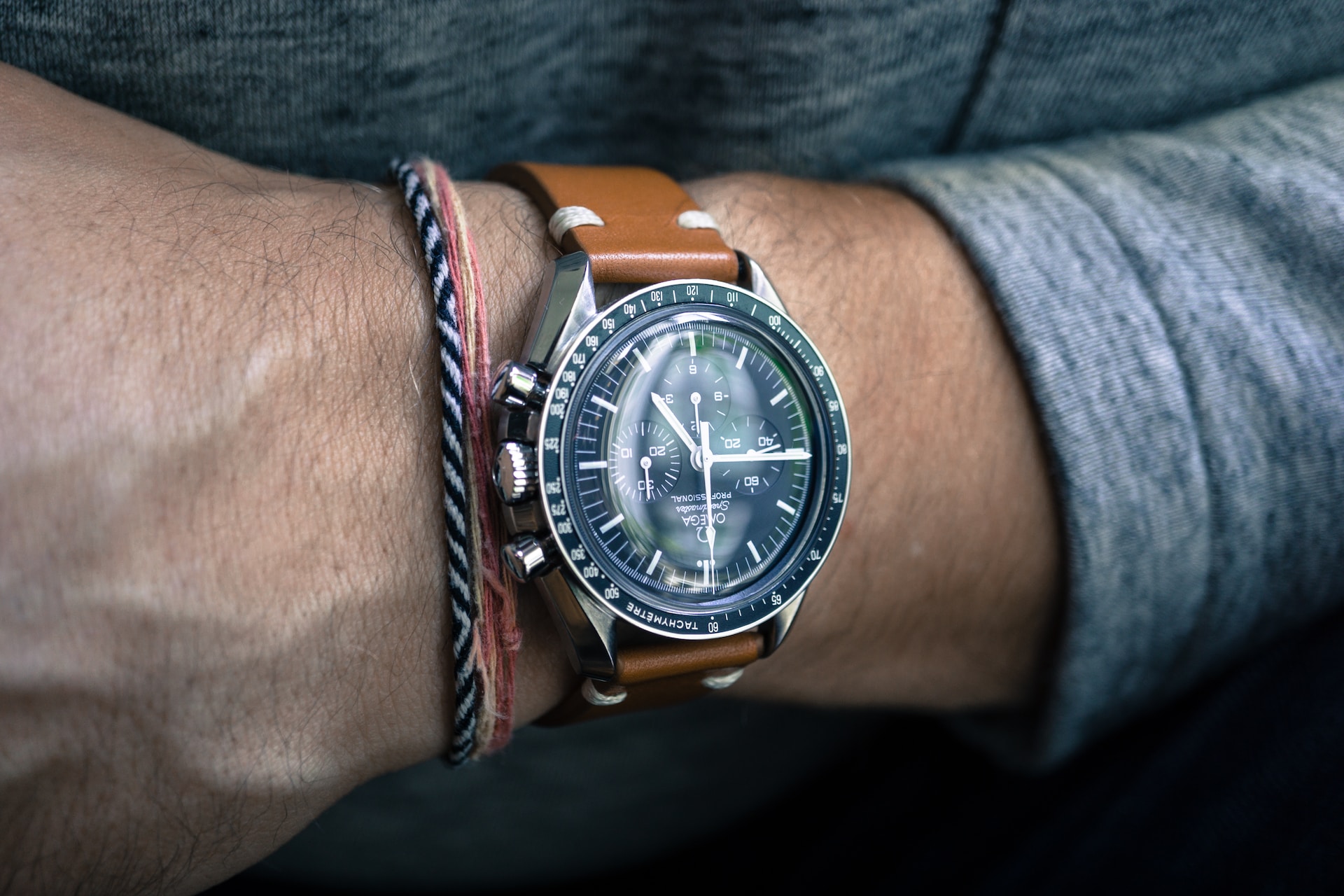A person wearing a round silver colored bezel chronograph watch with a brown leather strap